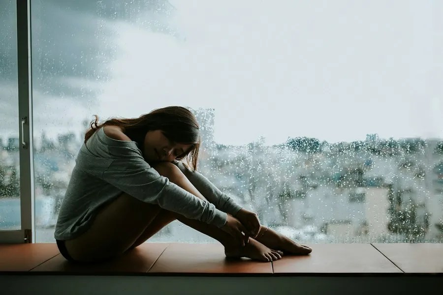 Person sitting with head down by a window, representing depression and low mood