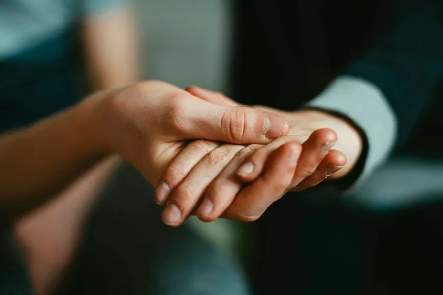 Hands gently holding another hand, representing trauma-informed support